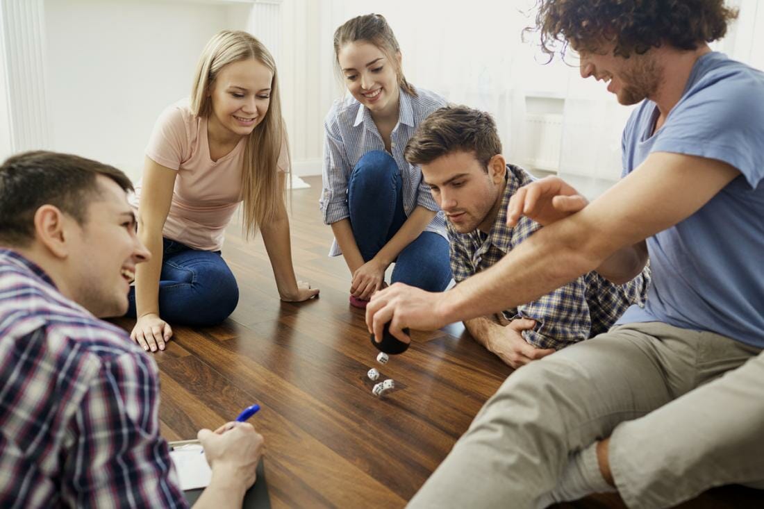 A group of friends play board games on the floor indoors